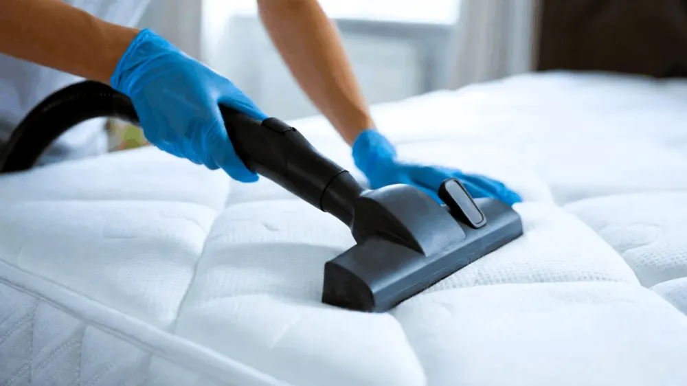 Limpieza y desinfección delicada de colchón blanco por técnico profesional con guantes para eliminar gérmenes y proteger la salud respiratoria